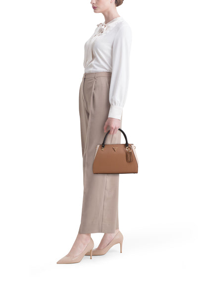 Sac à main beige de Guess, avec poignée noire et breloque décorative, porté avec un chemisier blanc et un pantalon assorti.
