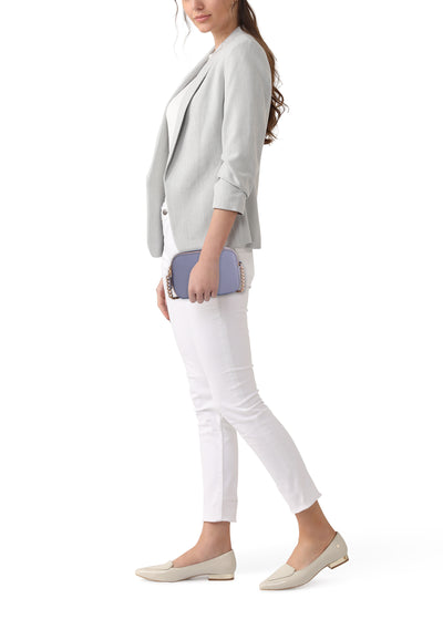 Sac à bandoulière bleu de Guess, avec chaîne dorée, porté avec un blazer gris et un pantalon blanc.