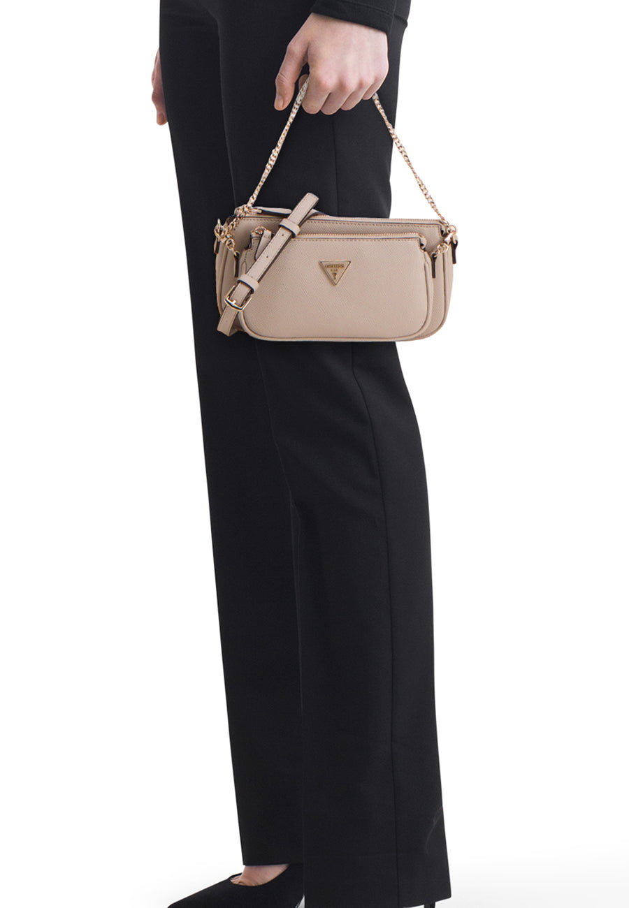 Sac à bandoulière beige de Guess, porté à la main par une chaîne dorée, avec une bandoulière ajustable et une tenue noire.
