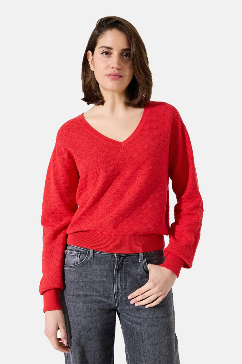 Pull rouge à col en V de GARCIA, avec une texture ajourée et porté avec un jean gris.