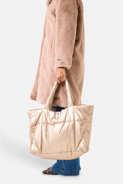 Sac à bandoulière doré de GARCIA, matelassé, porté avec un manteau texturé rose et des chaussures à motif léopard.
