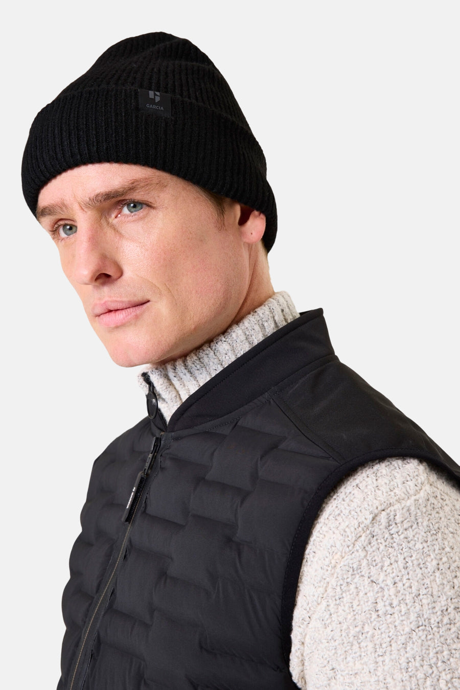 Zwarte GARCIA muts, van ribgebreid met een klein discreet logo, gedragen met een wollen trui en een zwart mouwloos vest.