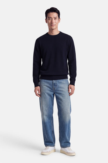 Pull col rond bleu marine par INDIGOLD, coupe ajustée, porté avec jeans délavés et baskets blanches, vue de face.