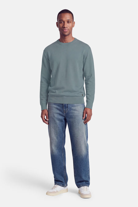Pull col rond bleu marine par INDIGOLD, coupe ajustée, manches longues, bord-côte aux poignets et ourlet, porté avec jeans délavés et baskets blanches, vue de face.