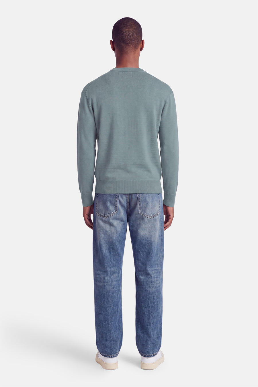 Pull col rond bleu clair de INDIGOLD, vue dos, avec finition côtelée aux manches et ourlet, porté avec jeans délavés et baskets blanches.