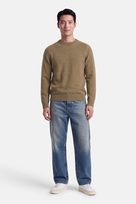 Pull col rond beige par INDIGOLD, en maille fine, porté avec jeans délavés et baskets blanches, vue de face.