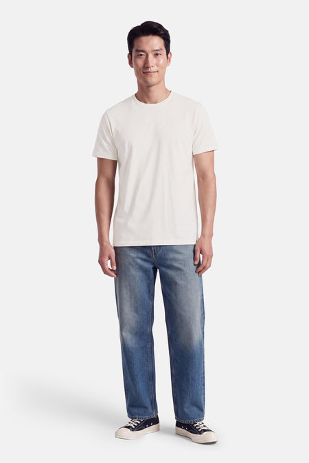 T-shirt blanc à manches courtes de coupe classique par INDIGOLD, porté avec jeans bleus et baskets noires, vue frontale.