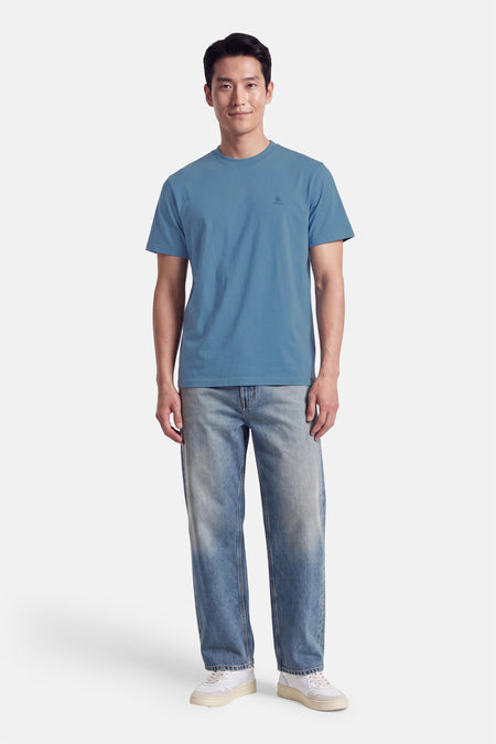 T-shirt bleu à manches courtes par INDIGOLD, coupe droite, col rond, petit logo discret sur la poitrine, porté avec jeans délavés et baskets blanches.