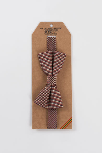 Paarse vlinderdas geweven door Le Fabuleux Marcel de Bruxelles, bordeauxrood en beige geruit patroon, op zijn kartonnen verpakking.