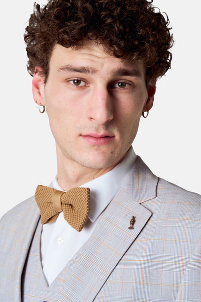 Blazer brun à carreaux par Le Fabuleux Marcel de Bruxelles, avec nœud papillon en tricot et broche décorative.