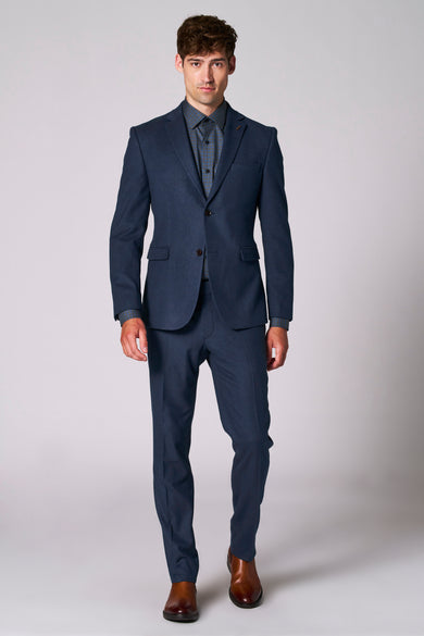 Blazer bleu de Le Fabuleux Marcel de Bruxelles, porté avec une chemise à carreaux, et des chaussures marron.
