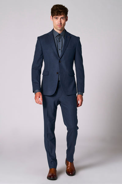 Blazer bleu de Le Fabuleux Marcel de Bruxelles, porté avec une chemise à carreaux, et des chaussures marron.
