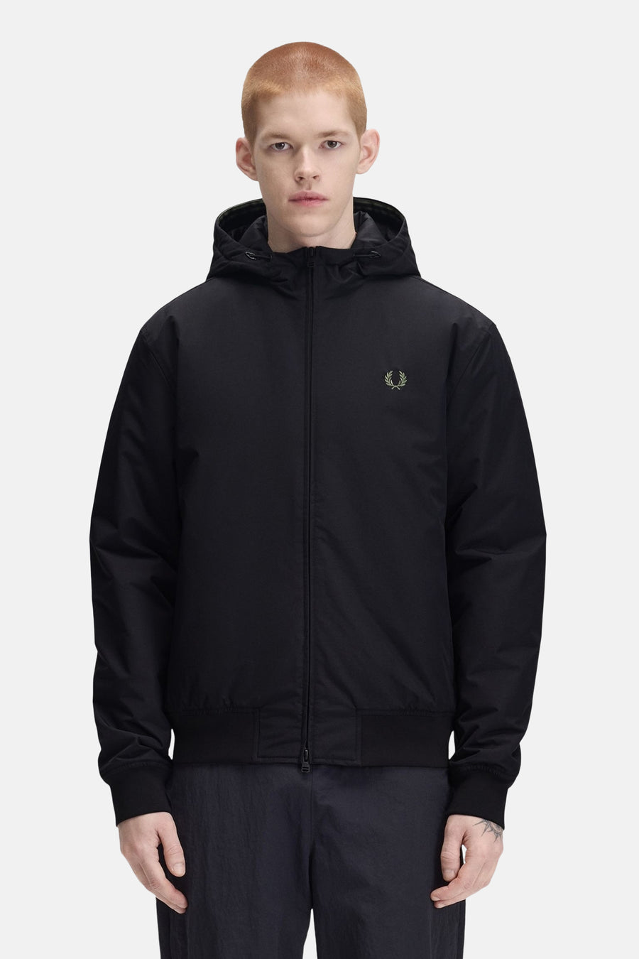 Black hooded waterproof jacket by Fred Perry with olive green laurel wreath logo, front zip closure, and elastic cuffs, shown in front view on model.