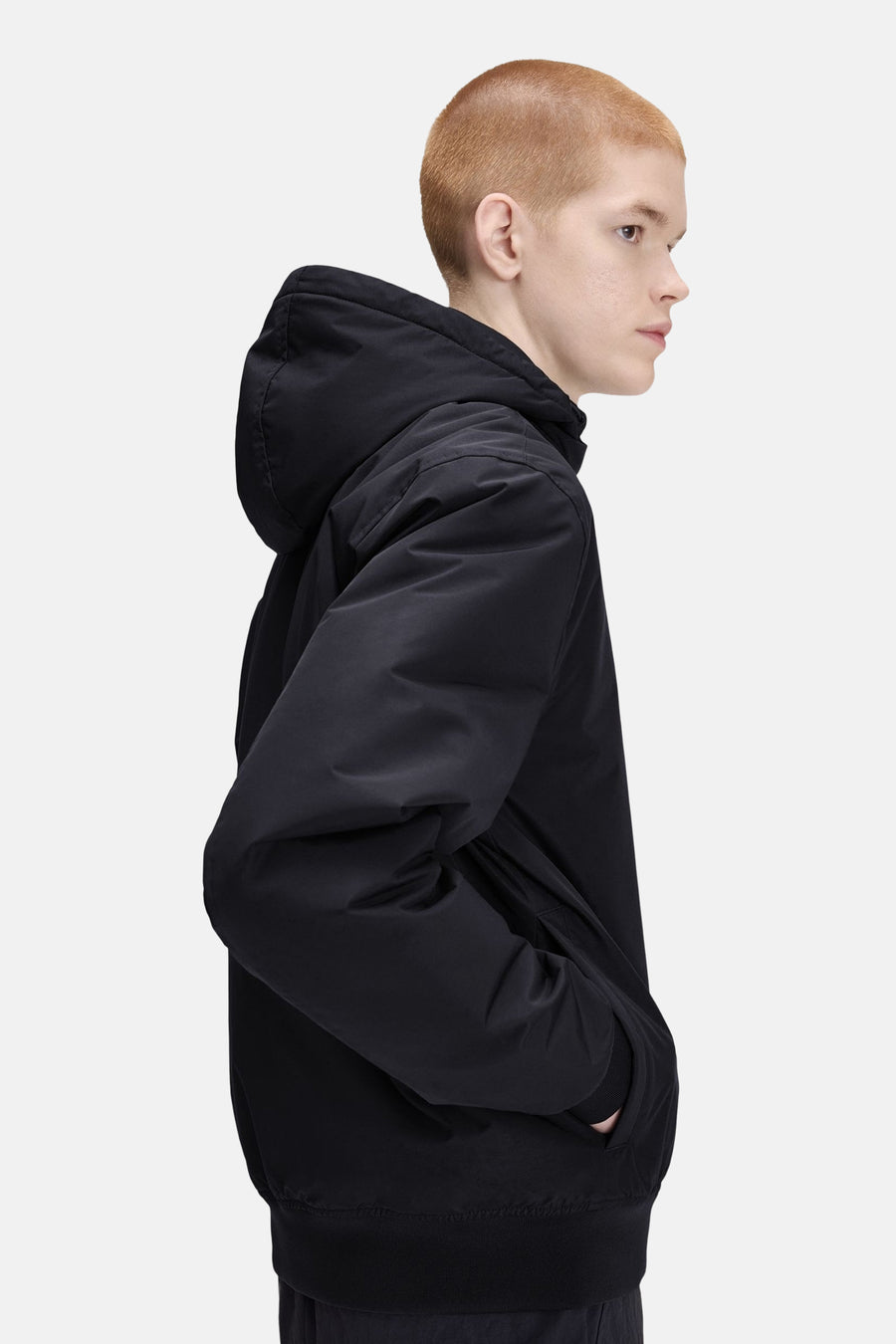 Black hooded waterproof jacket side view with ribbed hem and front pockets, worn by model with short hair