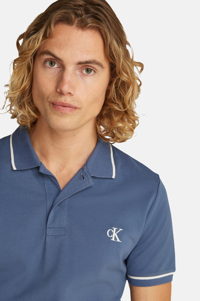 Blauw poloshirt van Calvin Klein, met een geborduurd logo op de borst en witte afwerkingen aan de mouwen en kraag.