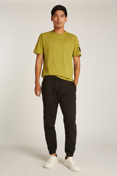 Okerkleurig T-shirt met korte mouwen van Calvin Klein, gedragen met een zwarte joggingbroek en witte sneakers.