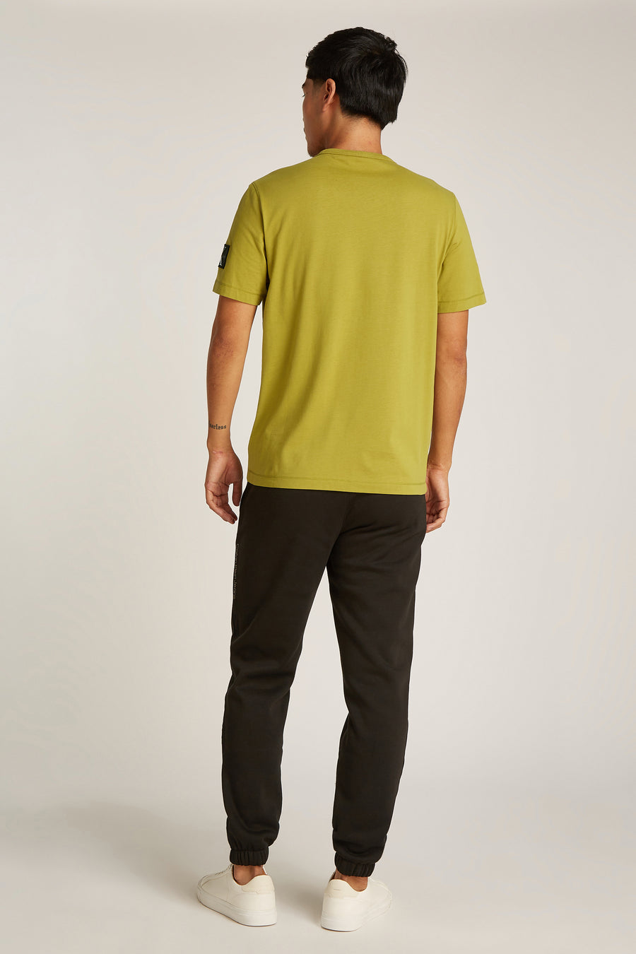 Okerkleurig T-shirt met korte mouwen van Calvin Klein, gedragen met een zwarte broek en witte sneakers, achtergezicht.