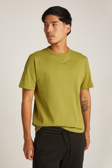 Okerkleurig T-shirt met korte mouwen van Calvin Klein, gedragen met een zwarte joggingbroek.