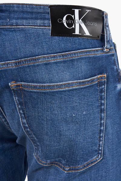 Jean slim en denim bleu foncé de Calvin Klein avec surpiqûres contrastées et patch logo noir à l'arrière.