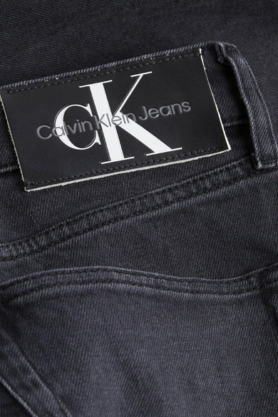Jean fuselé gris foncé de Calvin Klein avec étiquette de marque en cuir noir sur la taille.