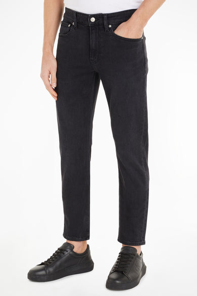 Jean tapered gris foncé de Calvin Klein, porté avec des chaussures de sport noires.
