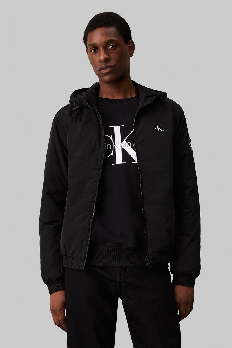 Imperméable noir de Calvin Klein, porté par un homme, avec capuche et fermeture éclair visible.