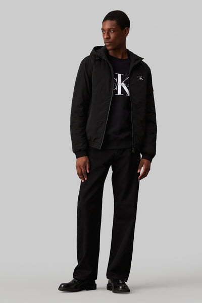 Imperméable noir par Calvin Klein, porté avec un t-shirt noir à logo et un pantalon noir.
