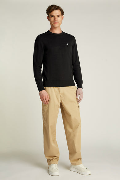 Pull col rond noir de Calvin Klein, porté avec un pantalon cargo beige et des chaussures blanches.