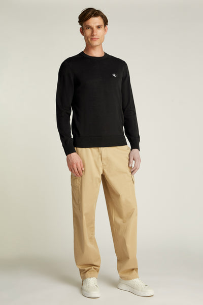 Pull col rond noir de Calvin Klein, porté avec un pantalon cargo beige et des chaussures blanches.