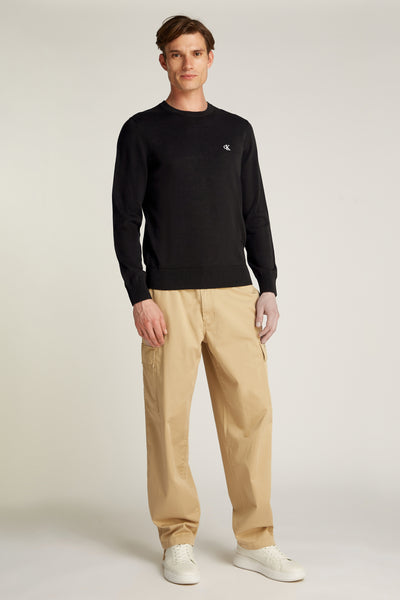 Pull col rond noir de Calvin Klein, porté avec un pantalon cargo beige et des baskets blanches.