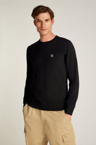 Pull col rond noir de Calvin Klein, porté avec un pantalon cargo beige.