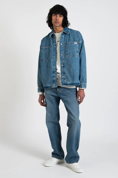 Chemise en jean bleu moyen de Calvin Klein, portée ouverte sur un t-shirt blanc et un pantalon en jean assorti.