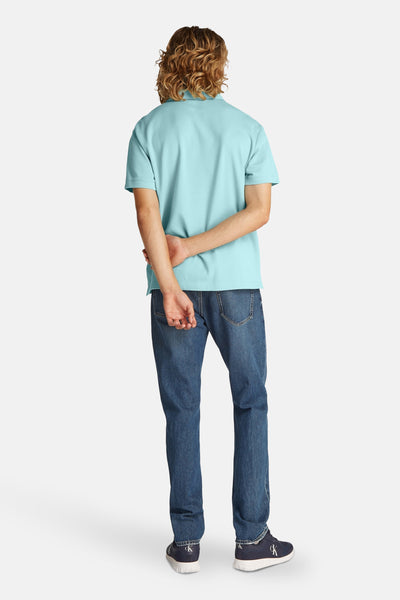 Turquoise poloshirt met korte mouwen van Calvin Klein, gedragen met een blauwe spijkerbroek en marineblauwe sneakers, achtergezicht.
