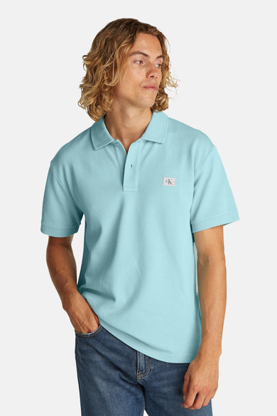Turquoise poloshirt met korte mouwen van Calvin Klein, gedragen met een blauwe spijkerbroek en golvend blond kapsel.