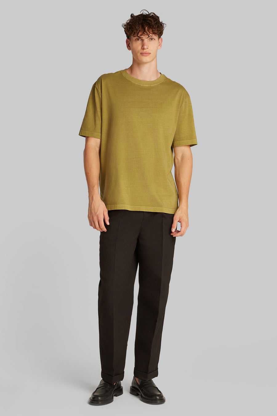 Okerkleurig T-shirt met korte mouwen van Calvin Klein, gedragen met een zwarte broek en loafers.