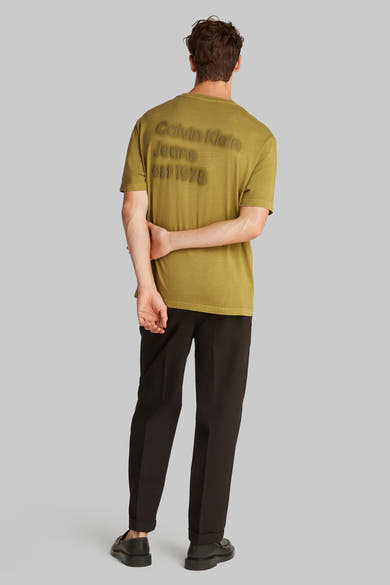 Okerkleurig T-shirt met korte mouwen van Calvin Klein met het merklogo op de rug, gedragen met een zwarte broek.