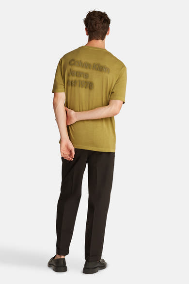 Okerkleurig T-shirt met korte mouwen van Calvin Klein Jeans, met reliëf logo op de rug, gedragen met een zwarte broek.