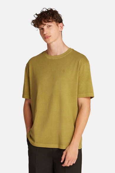 Okerkleurig T-shirt met korte mouwen van Calvin Klein, gedragen met een zwarte broek, handen in de zakken.