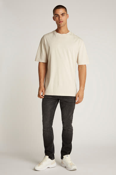 Ecru T-shirt met korte mouwen van Calvin Klein, gedragen met een zwarte jeans en witte sneakers.