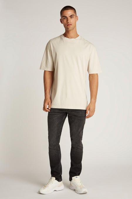 Ecru T-shirt met korte mouwen van Calvin Klein, gedragen met een zwarte jeans en witte sneakers.