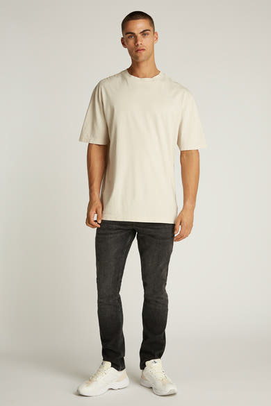 Ecru T-shirt met korte mouwen van Calvin Klein, gedragen met een zwarte jeans en witte sneakers.