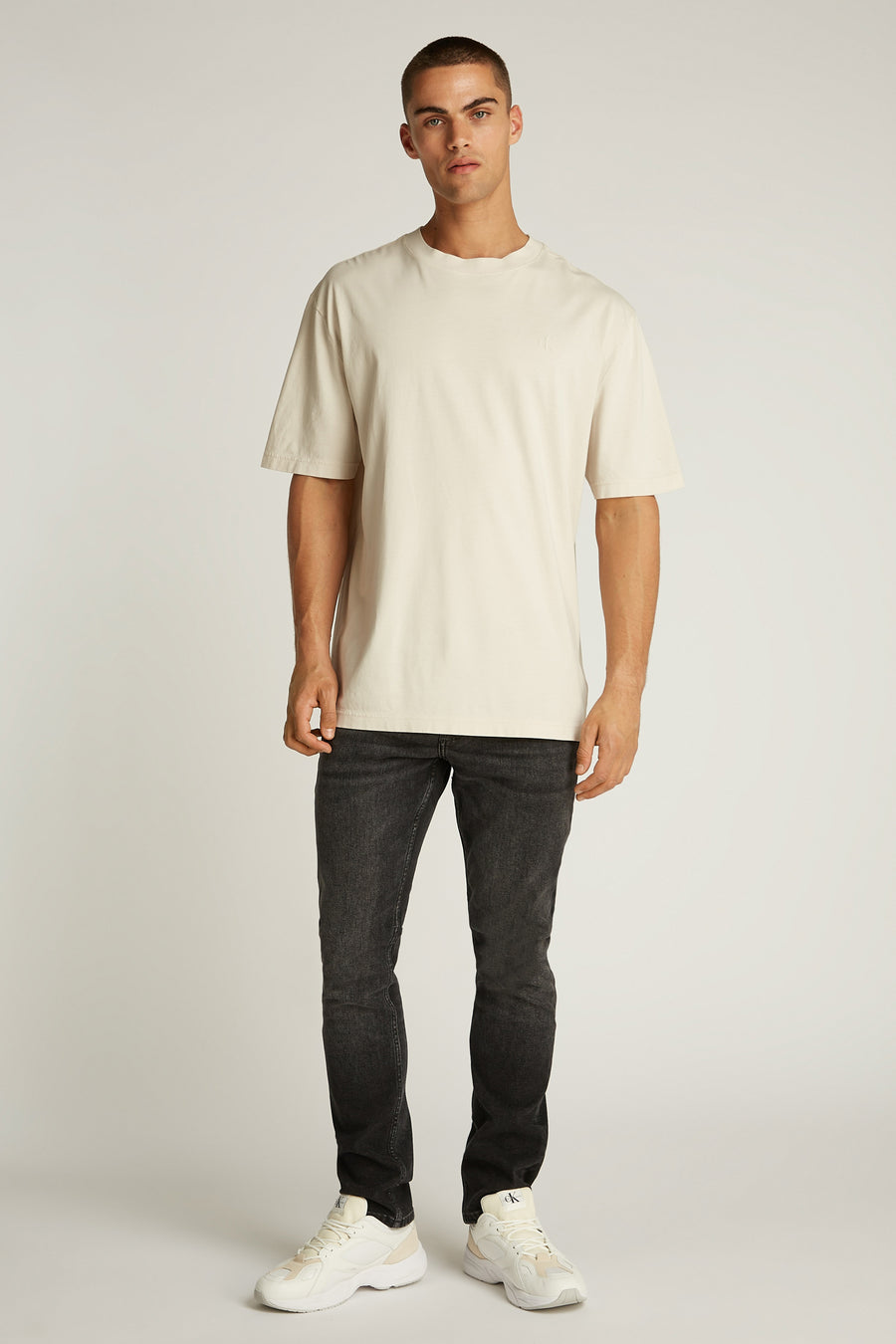 Ecru T-shirt met korte mouwen van Calvin Klein, gedragen met een zwarte jeans en witte sneakers.