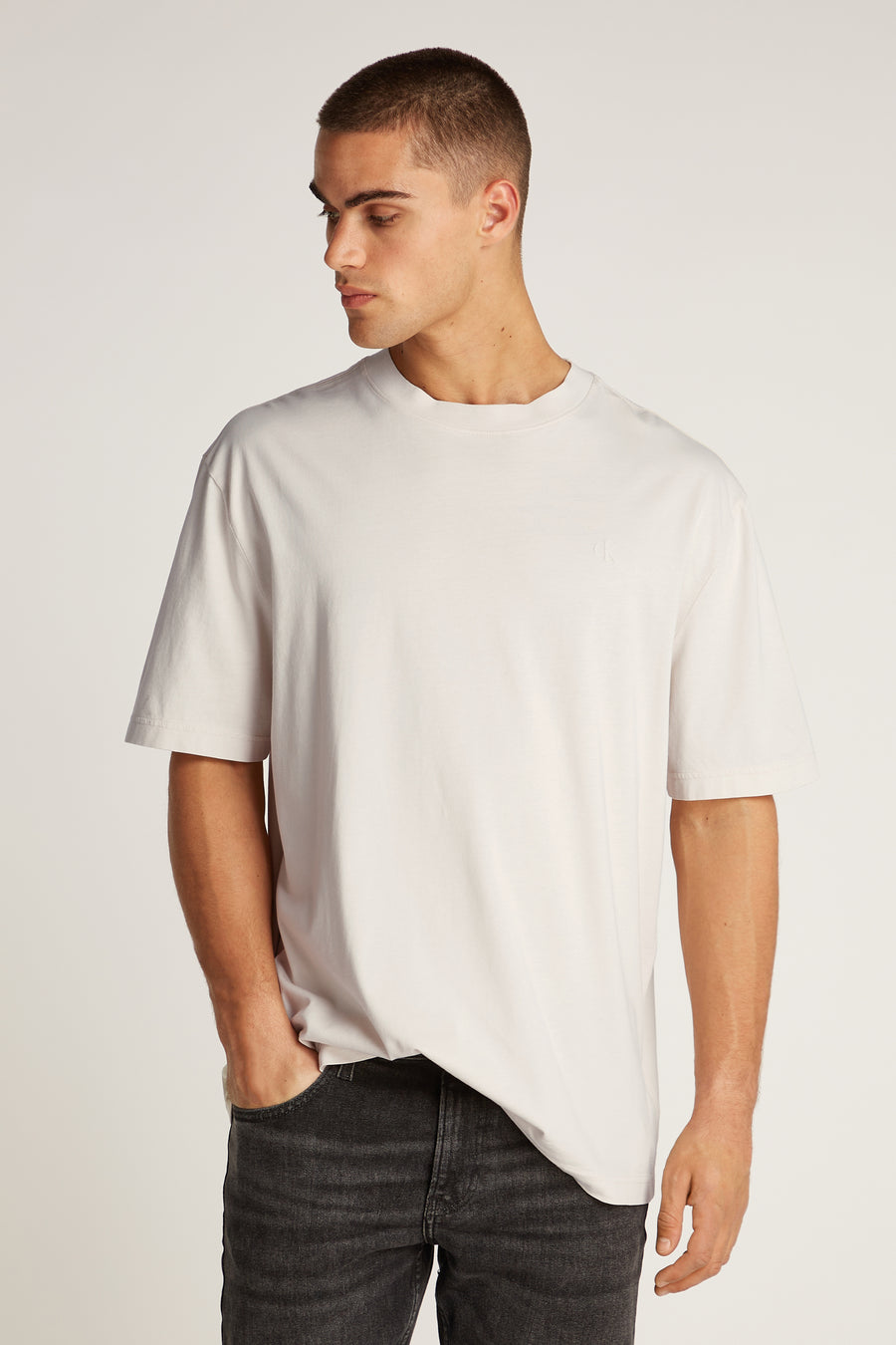 Ecru T-shirt met korte mouwen van Calvin Klein, gedragen met een zwarte, uitgewassen spijkerbroek, model kijkt naar links.