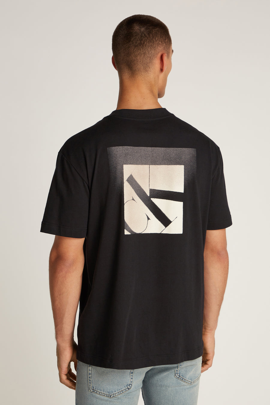 Zwart T-shirt met korte mouwen van Calvin Klein, met vierkant grafisch patroon op de rug, gedragen met een spijkerbroek.