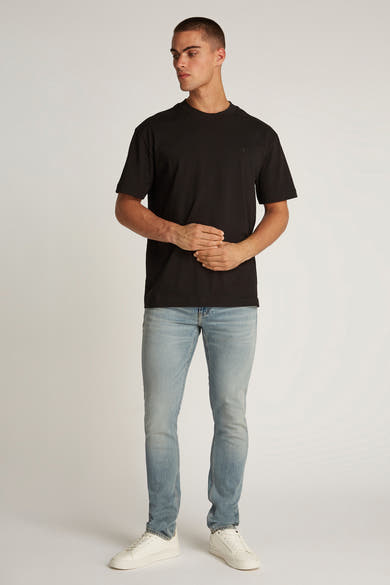 Zwart T-shirt met korte mouwen van Calvin Klein, gedragen met een lichte spijkerbroek en witte sneakers.