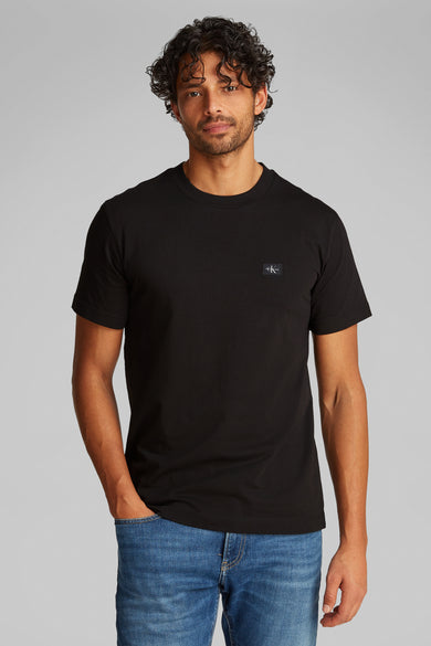Zwart T-shirt met korte mouwen van Calvin Klein, gedragen met een blauwe spijkerbroek en grijze sneakers.
