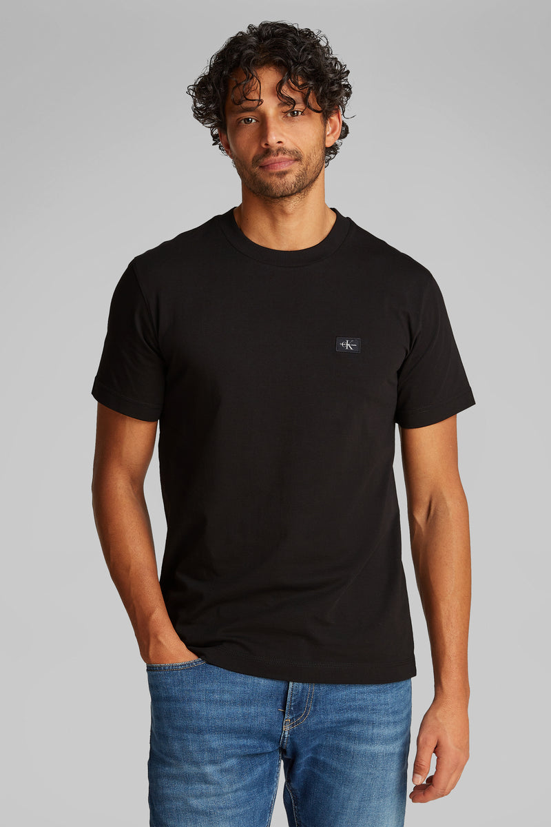 Zwart T-shirt met korte mouwen van Calvin Klein, gedragen met een blauwe spijkerbroek en grijze sneakers.