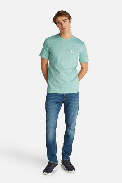 Turquoise T-shirt met korte mouwen van Calvin Klein, gedragen met een blauwe spijkerbroek en marineblauwe sneakers.