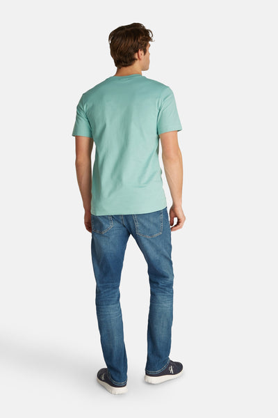 Turquoise T-shirt met korte mouwen van Calvin Klein, gedragen met een blauwe spijkerbroek en marineblauwe schoenen.