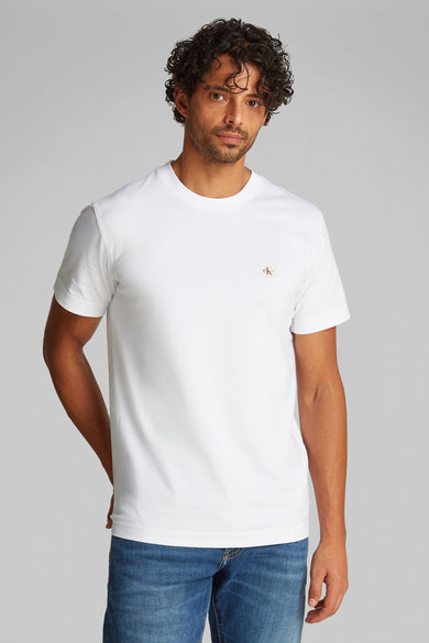 Wit T-shirt met korte mouwen van Calvin Klein, gedragen met een blauwe spijkerbroek en grijze sneakers.